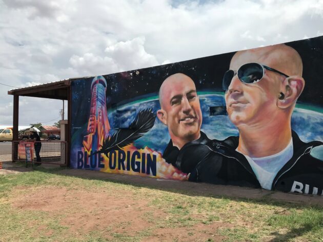 De ruimteopnamen van Blue Origin geven het kleine stadje in Texas een boost die groter is dan verwacht  Een muurschildering geschilderd op een gebouw dat te koop staat in Van Horn, Texas, toont Jeff Bezos en zijn broer Mark, die dinsdag in het suborbitale ruimteschip van Blue Origin zullen rijden. (GeekWire-foto / Alan Boyle) VAN HORN, Texas — Toen ik deze stad in West-Texas voor het laatst in 2006 bezocht, was de ruimtevaartonderneming Blue Origin van Jeff Bezos van plan om tegen 2010 suborbitale ruimtereizen aan te bieden voor betalende passagiers . Het slechte nieuws voor Van Horn is dat het tien jaar langer heeft geduurd dan verwacht voordat de ruimtevaart van Blue Origin naar Van Horn kwam. Maar het goede nieuws is dat de economische impact aantoonbaar tien keer zo groot is. De 15 jaar oude milieubeoordeling van Blue Origin, die het onderwerp was van de hoorzitting van de Federal Aviation Administration die ik in 2006 bijwoonde, schatte dat 20 tot 35 voltijdse werknemers zouden werken op de suborbitale lanceerbasis van het bedrijf, een halfuur rijden ten noorden van Van Hoorn. Vijftien jaar later is het werkelijke aantal 275 werknemers – niet alleen vanwege het suborbital-ruimteschip New Shepard van Blue Origin, dat Bezos en drie bemanningsleden dinsdag zullen besturen, maar ook vanwege het testprogramma voor raketmotoren dat is gebaseerd op Launch Site One. De BE-3-motoren die op New Shepard worden gebruikt, worden gebouwd in het hoofdkantoor van Blue Origin in Kent, Washington, maar worden in Texas tot in de puntjes uitgeprobeerd. Launch Site One is ook de testsite voor de krachtigere BE-4-raketmotoren van Blue Origin.  Patricia Golden, directeur van Van Horn's Clark Hotel Museum, pronkt met een schaalmodel van Blue Origin's New Shepard suborbital raketschip. (GeekWire-foto / Alan Boyle) Het personeelsbestand van Blue Origin in West-Texas vormt slechts een fractie van het totale personeelsbestand van Blue Origin van meer dan 3.500 mensen. Niettemin hebben 275 relatief goedbetaalde banen een impact op de 1.900 inwoners van Van Horn, en meer in het algemeen op Culberson County. "Ze zijn een van de grotere belastingbetalers in het graafschap – niet alleen de stad, maar het graafschap", vertelde Van Horn-burgemeester Becky Brewster me. En dat is voordat Blue Origin echte passagiers begon te vliegen. "Dit is wat het moment van geschiedenis zal zijn," zei Brewster. "We verwachten nog veel meer groei met betrekking tot dit nieuwe hoofdstuk in de relatie van Blue Origin met deze gemeenschap." Culberson County kan een boost gebruiken: het behoort doorgaans tot het laagste kwartaal van de 254 provincies van Texas als het gaat om het inkomen per hoofd van de bevolking, en naar schatting 19,7% van de bevolking leeft in armoede. In de afgelopen jaren zijn die cijfers in een positieve richting aan het evolueren , en het is moeilijk te beweren dat de werkgelegenheid van Blue Origin geen factor is. De impact is niet alleen voelbaar in de werkgelegenheidsstatistieken: Brewster zei dat Blue Origin ook met ontwikkelaars heeft samengewerkt om meer woningen te bouwen in het Van Horn-gebied. Brewster zei dat ongeveer 40% van de werknemers van het bedrijf in West-Texas Van Horn specifiek opeisen als hun woonplaats. Van de medewerkers van Blue Origin is bekend dat ze roboticalessen geven op lokale scholen, en het bedrijf heeft geholpen bij het ontwikkelen van een curriculum voor lucht- en ruimtevaarttechniek voor de Universiteit van Texas in El Paso, ongeveer 120 mijl naar het westen.  De tienjarige Gabriel Williams stopt een ansichtkaart in een raketvormige brievenbus die wordt gebruikt voor het programma 'Postcards to Space' van Club for the Future. (GeekWire-foto / Alan Boyle) Net buiten Van Horn's Clark Hotel Museum heeft Blue Origin een brievenbus geplaatst voor ansichtkaarten die naar de ruimte zullen worden gevlogen als onderdeel van een programma dat is opgezet door de Club for the Future , de educatieve non-profitstichting van het bedrijf. De raketvormige doos was deze week een magneet voor buurtbewoners. "Ik heb 20 ansichtkaarten gemaakt", vertelde de directeur van het museum, Patricia Golden, me. Meer dan een dozijn werden verkocht aan klanten die langskwamen tijdens de paar minuten die ik in het museum doorbracht. Golden verkoopt de ansichtkaarten evenals de zegels van 36 cent die moeten worden aangebracht om de kaarten terug te sturen naar hun afzenders. 'Ik wilde postzegels met Amerikaanse vlag, om te laten zien dat het Amerika is,' zei ze, maar die postzegels hebben niet de juiste waarde. Niet alles aan de aanwezigheid van Blue Origin is aantrekkelijk. Golden klaagde dat hotelkamers in Van Horn moeilijk te vinden waren voor de Frontier Days en Jubilee-reünie van deze week, vanwege alle buitenstaanders die op bezoek waren voor de lancering van dinsdag. "Ik ben niet blij met al deze gekke dingen," zei ze. "Ik ben hierheen verhuisd omdat het Podunk is ." Burgemeester Brewster is ook op zijn hoede over het tempo van de vooruitgang. Ze vertelde me dat ze liever een langzame en gestage groei zou zien in plaats van een kortstondige hausse in het bedrijfsleven – en dat past perfect bij het standpunt van Bezos. Een van de favoriete uitspraken van de miljardair is "langzaam is soepel en soepel is snel." En de mascotte van Blue Origin, die meer dan 15 jaar teruggaat, is een langzame en gestage schildpad . Hoe ziet Van Horn er over 15 jaar uit? Ik kan niet wachten om erachter te komen.